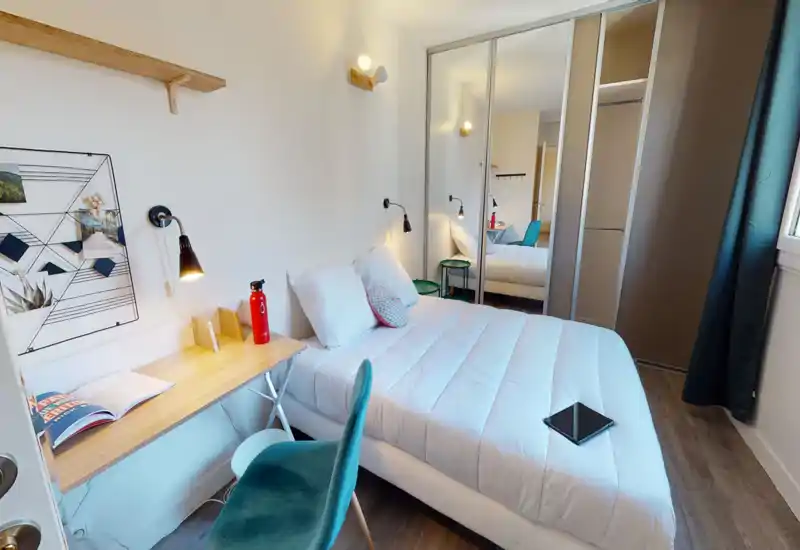Bright, modern single bedroom with a neatly made double bed, bedside lamps, a small desk and chair, and mirrored sliding wardrobes that add depth and storage.