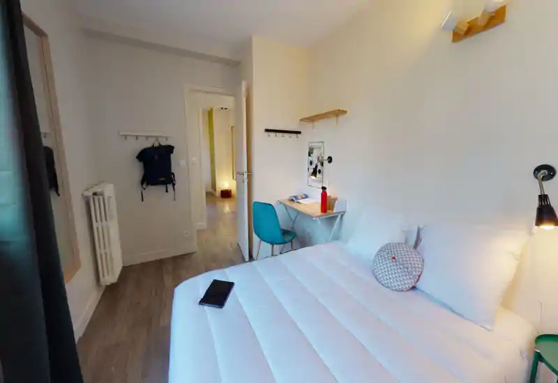 Clean, well-lit bedroom with a comfortable double bed, bedside lamps and a small desk with chair — ideal for rest and light work.