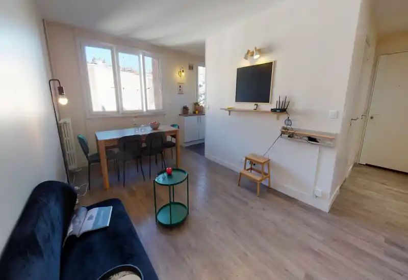 Salon moderne et lumineux avec canapé en velours, petite table basse verte et table à manger près de grandes fenêtres qui apportent beaucoup de lumière naturelle.