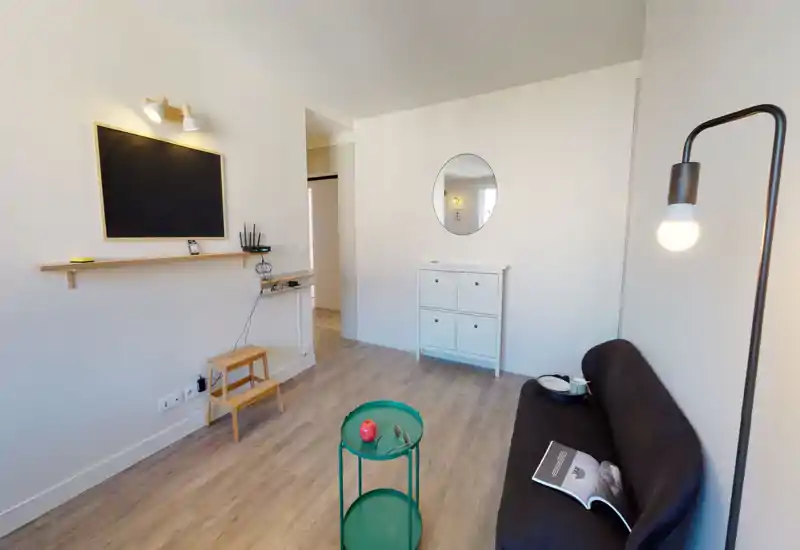 Espace de vie lumineux et minimaliste avec canapé compact, lampe sur pied et petite table ronde — décoration sobre style scandinave et parquet clair pour une ambiance accueillante.