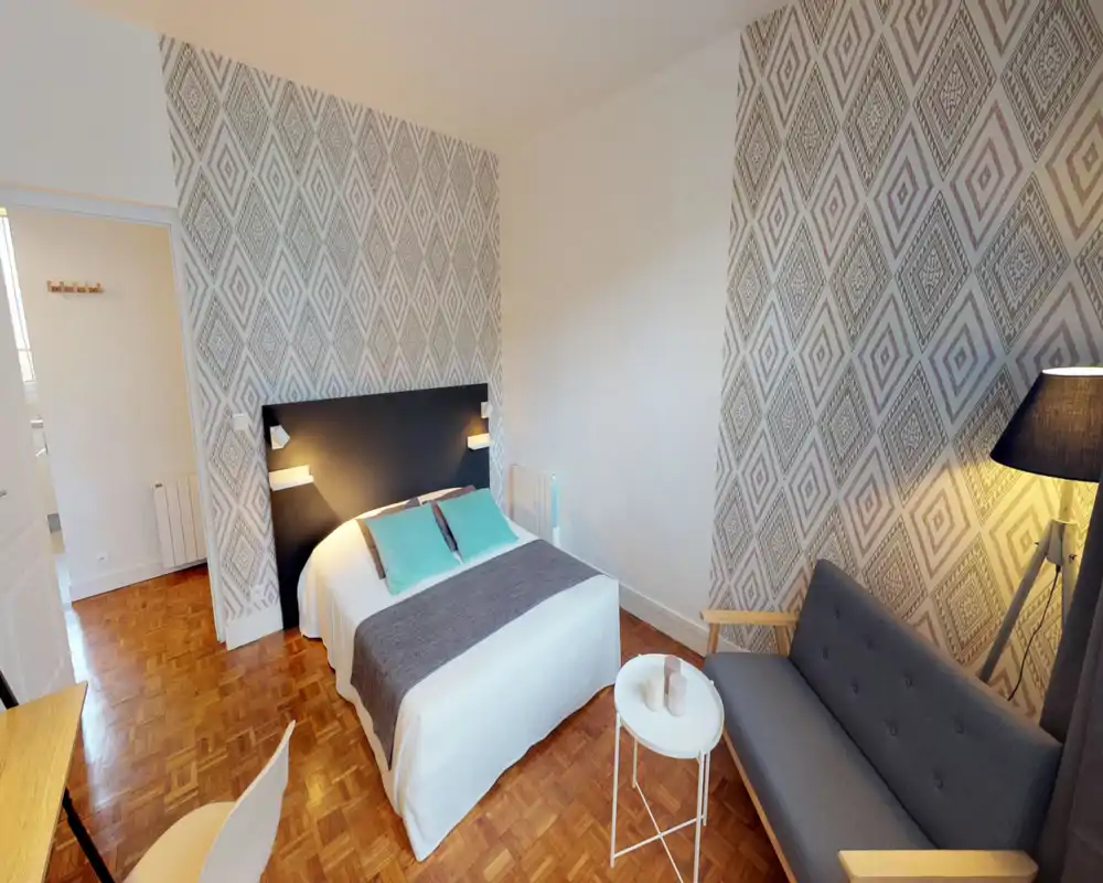 Chambre lumineuse et stylée avec lit double, papier peint graphique, petit canapé et lampes de chevet — mise en scène soignée et accueillante.