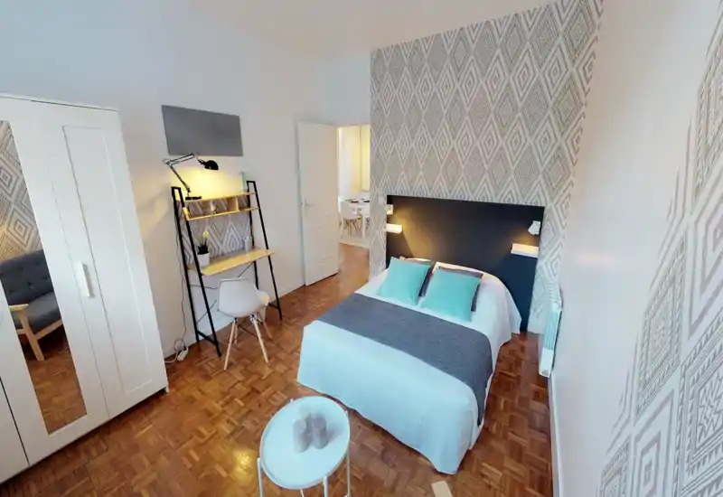 Chambre lumineuse et élégante avec lit double, mur à motif, bureau avec chaise, armoire et textiles confortables — idéale pour un séjour agréable.