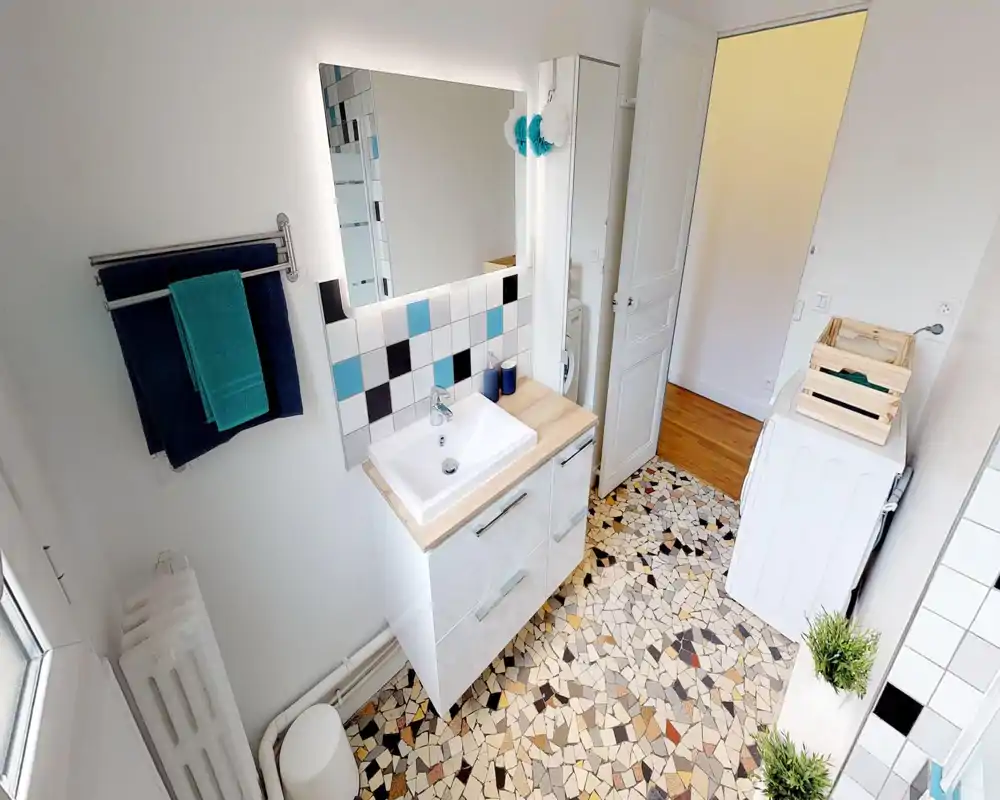 Bright, modern bathroom with a vanity sink, illuminated mirror, towel rack and patterned terrazzo-style floor tiles. The space is tidy and well lit, ideal for rental photos.