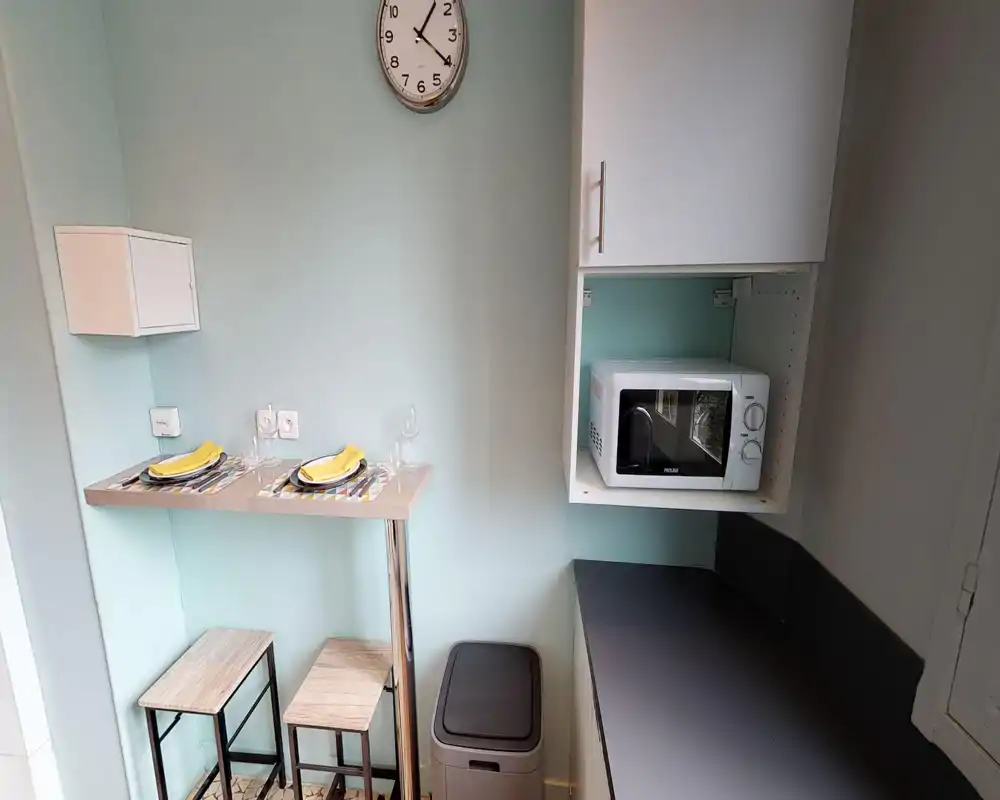 Compact kitchenette with a microwave, breakfast bar and two stools. Pale aqua walls and coordinated placemats create a fresh, tidy look ideal for short stays.