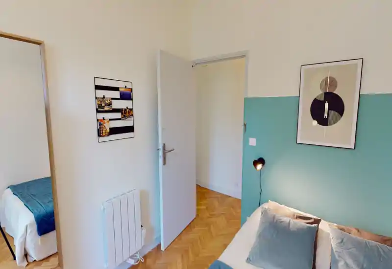 Angolo camera accogliente e ben arredato con letto ordinato, cuscini morbidi e parete accentata color teal. La luce naturale e il pavimento in parquet rendono l’ambiente caldo e invitante — perfetto per annunci di affitto.