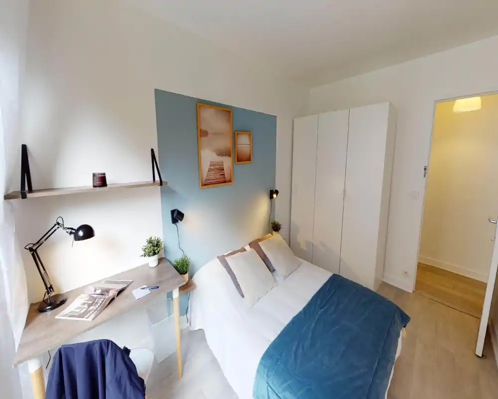 Camera da letto luminosa e ben arredata con letto matrimoniale, parete d'accento blu e lampade da comodino. Una scrivania vicino alla finestra e un armadio bianco completano la disposizione pratica e accogliente.
