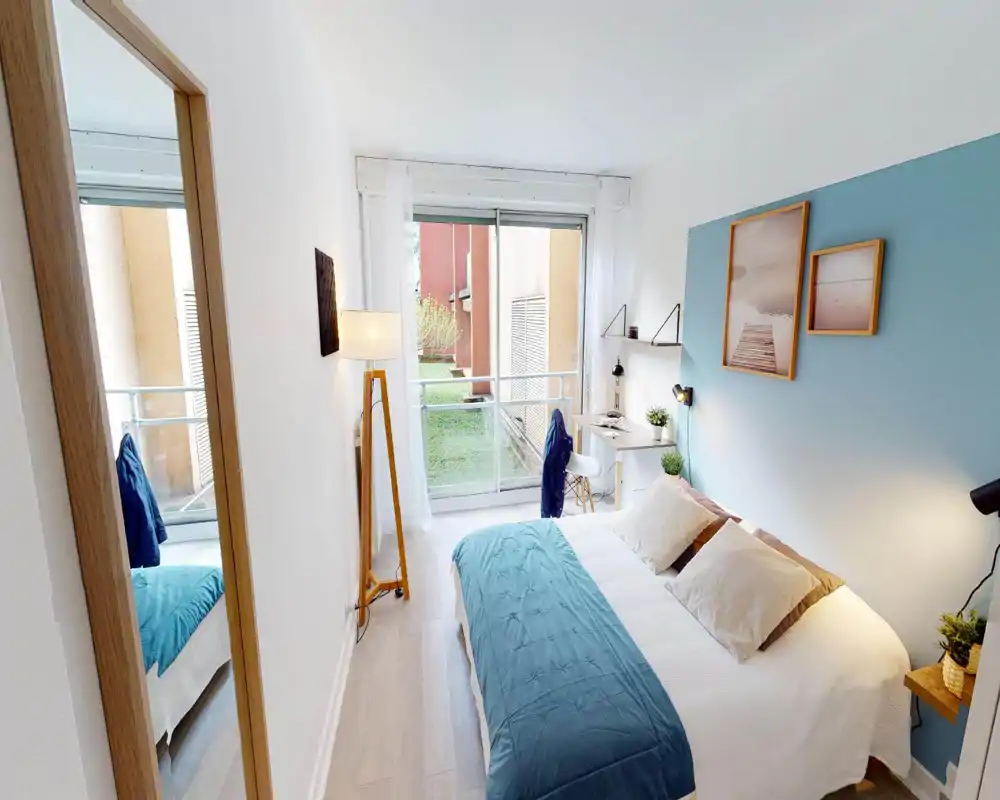 Camera da letto luminosa e moderna con letto matrimoniale rifatto, parete accentata azzurra, lampade da comodino e scrivania vicino alla porta finestra con vista sul giardino.