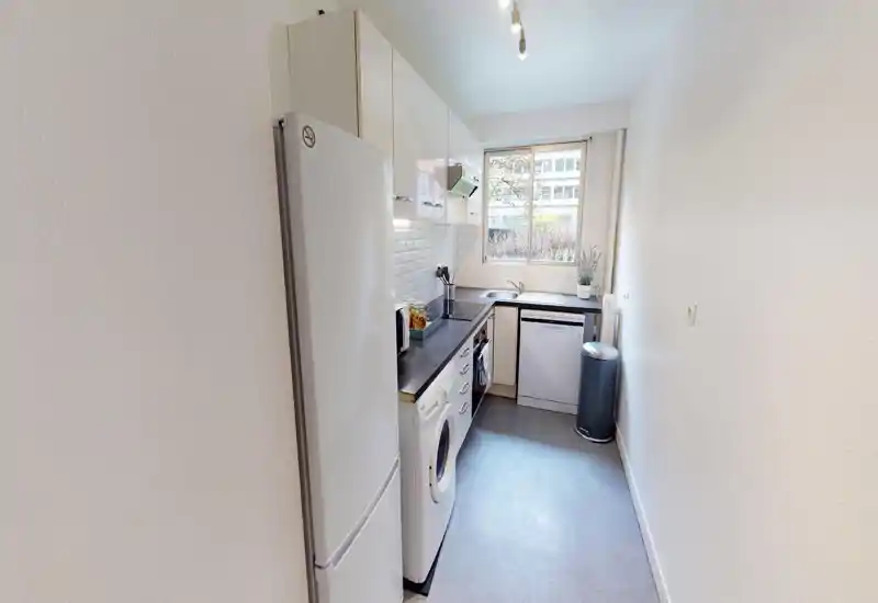 Bright, compact galley kitchen with modern white cabinets, black countertops, built-in appliances and a window providing natural light.