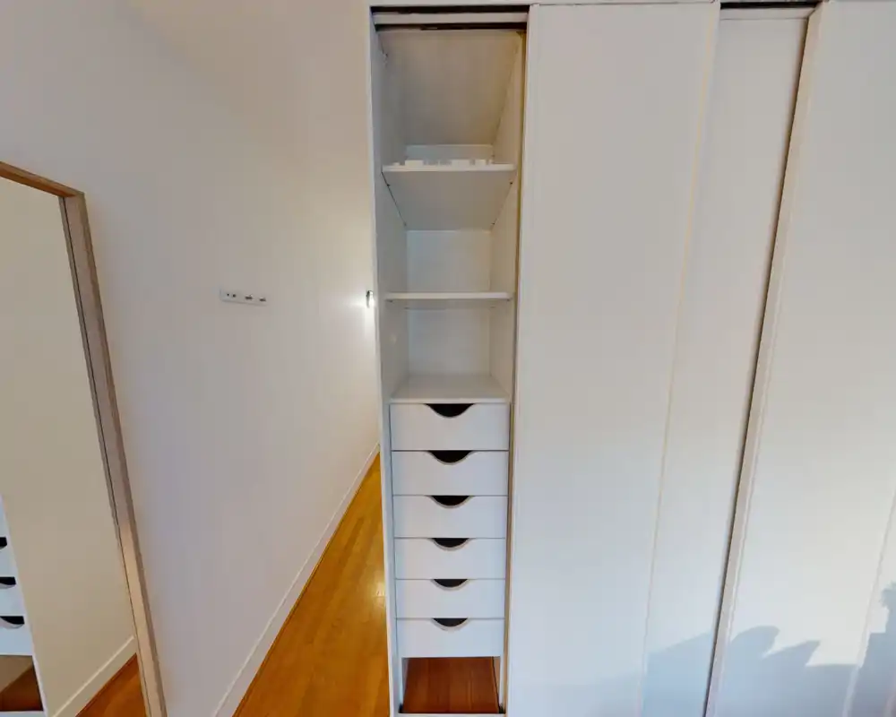 Gros plan sur une armoire encastrée avec tiroirs et étagères dans un couloir étroit ; la photo met l'accent sur le rangement plutôt que sur une pièce identifiable.