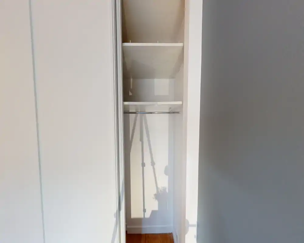 Petit placard encastré avec étagères et tringle, vide et bien éclairé — pratique pour présenter l'espace de rangement.