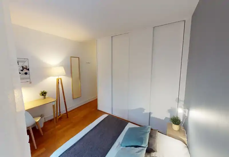Chambre lumineuse et bien mise en scène avec lit soigné, lampe de chevet et placards intégrés. L'éclairage chaud et le parquet apportent une ambiance cosy et moderne, idéale pour une annonce.