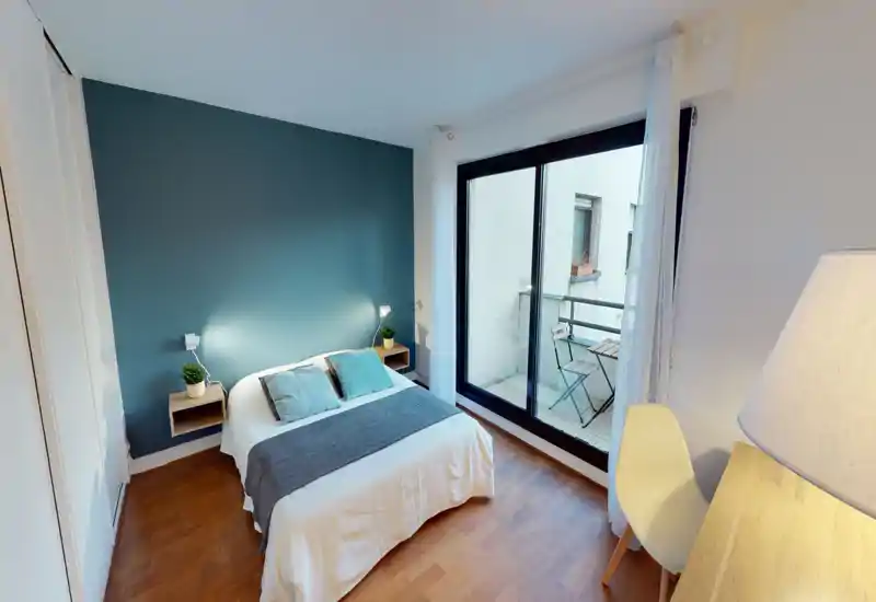 Chambre claire et soignée avec lit double, textiles doux et balcon. Coussins décoratifs, chevets flottants et mur d’accent bleu-vert créent une ambiance moderne et apaisante.
