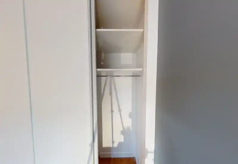 Petit placard encastré avec étagères et tringle, vide et bien éclairé — pratique pour présenter l'espace de rangement.