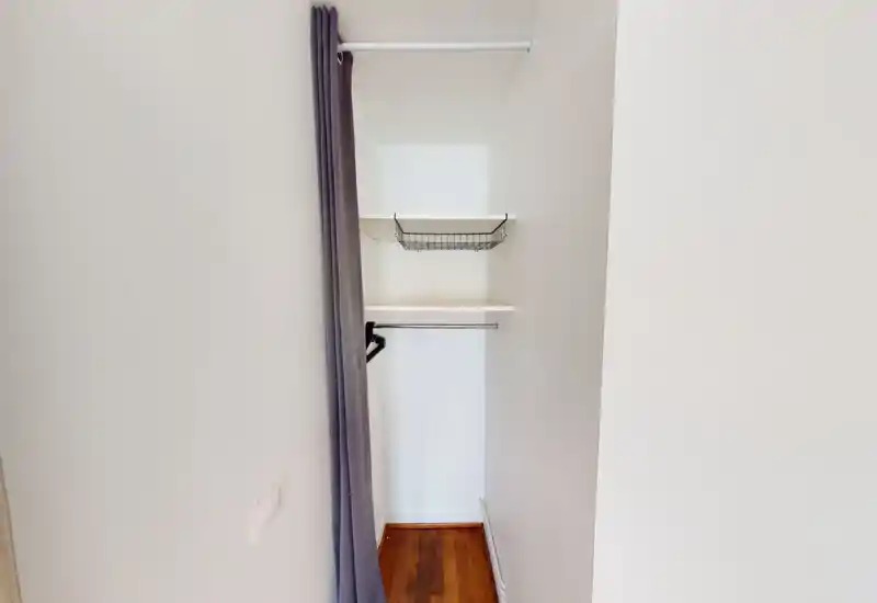 Petit placard/entrée avec tringle, étagère et panier métallique ; espace simple, lumineux et propre avec un rideau pour la confidentialité.