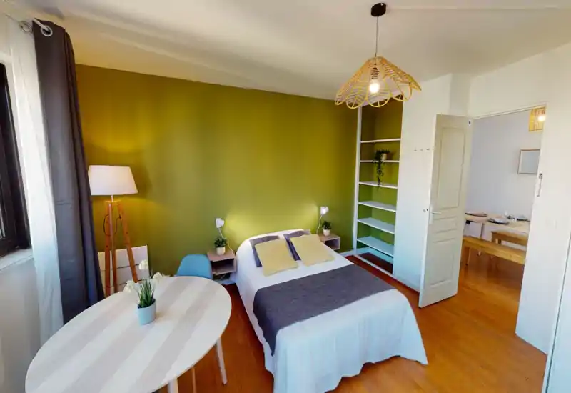 Bright, stylish bedroom with a double bed centered against an olive-green accent wall, cozy textiles, bedside shelves and natural light from the window.