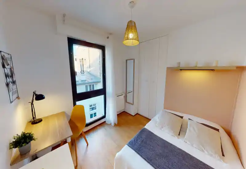 Chambre lumineuse et chaleureuse avec lit double, éclairage d'étagère chaleureux et un petit bureau près d'une grande fenêtre apportant beaucoup de lumière naturelle.