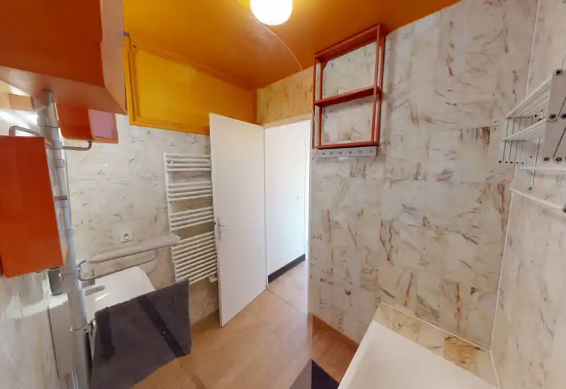 Clean, well-lit bathroom with marble-look tiled walls, a bathtub at lower right, a sink and towel radiator beside the open door.