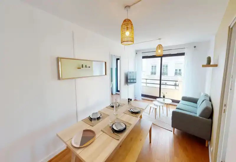 Bright, modern living room with a cozy sofa, coffee tables and a dining table set near a large balcony window — stylish wooden floors and warm pendant lights create a welcoming atmosphere.