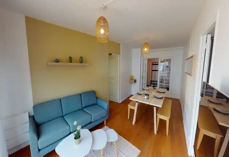 Bright, well-styled living room with a blue sofa, coffee tables and a dining area; warm wooden floors and pendant lamps create a cozy, modern atmosphere.