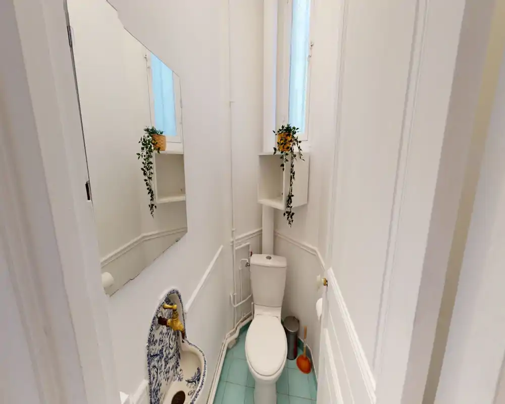 Petite salle de bains bien éclairée avec WC, lavabo mural décoratif et petites étagères ; murs blancs et carreaux turquoise clair pour une atmosphère propre et aérée.