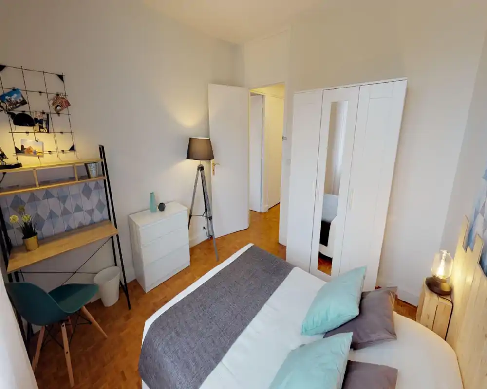 Camera da letto luminosa e ben arredata con letto matrimoniale in lino neutro e cuscini turchesi, armadio con specchio, lampada da comodino e una piccola area scrivania—ideale per soggiorni confortevoli.
