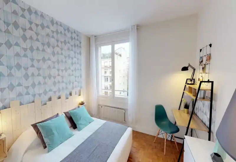 Bright, well-styled bedroom with a large bed, patterned accent wall and a small desk area by the window. Natural light and soft textiles make the room inviting for guests.