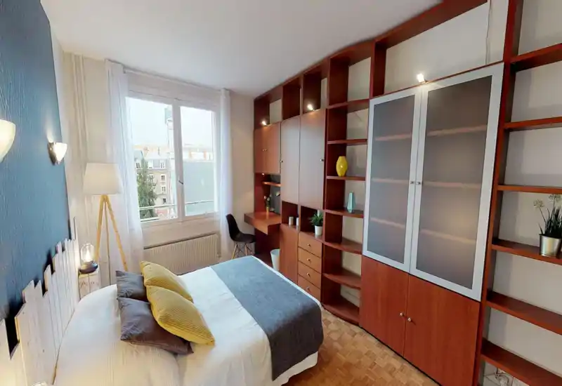 Camera da letto luminosa e ben arredata con letto matrimoniale, tessili coordinati e ampie scaffalature in legno con scrivania vicino alla finestra.