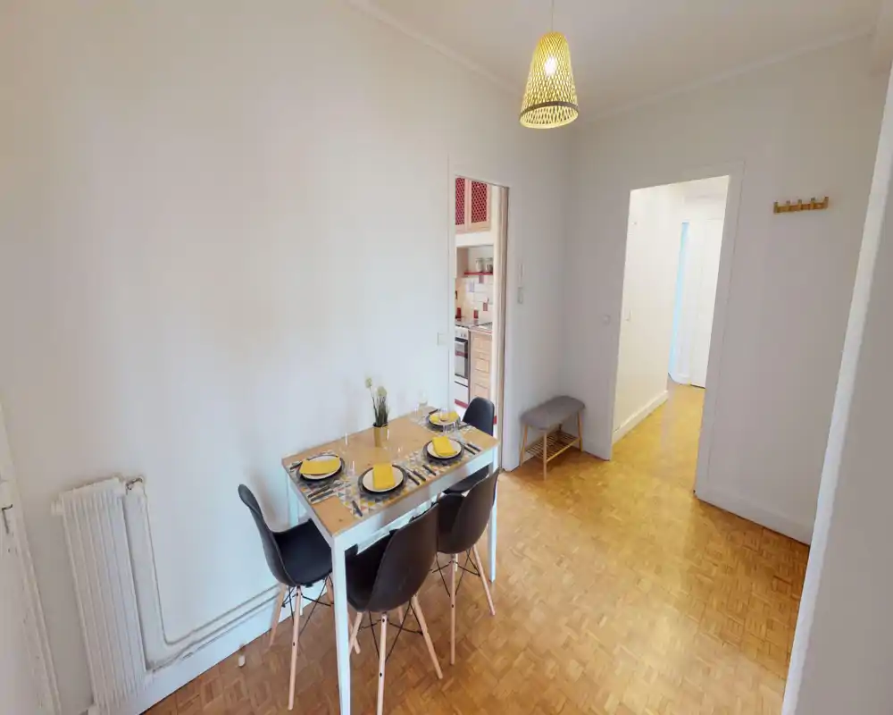Zona pranzo luminosa e curata con tavolo apparecchiato per quattro, sedie moderne e un caldo lampadario a sospensione — perfetta per pasti e piccoli ritrovi.