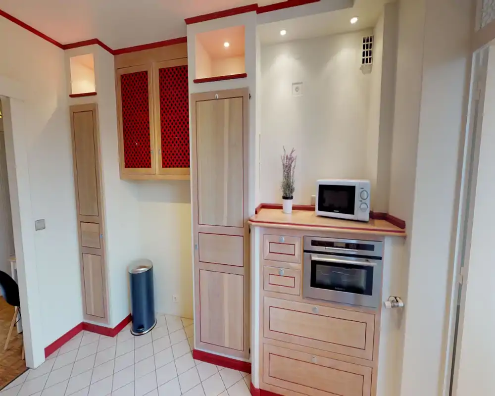 Angolo cottura compatto con mobili in legno integrati, forno e microonde. Piastrelle chiare e rifiniture rosse coordinano uno spazio funzionale e ordinato, ideale per soggiorni brevi.