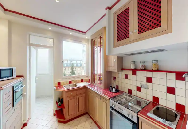 Cucina luminosa e ben arredata con mobili in legno e piastrelle rosse. Dotata di piano cottura a gas, lavello sotto una finestra ampia e vasetti decorativi che la rendono accogliente.