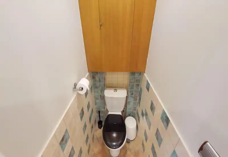 Bagno compatto e ben illuminato con vista ravvicinata sul WC, piastrelle fino a metà parete e un armadietto in legno sopra.
