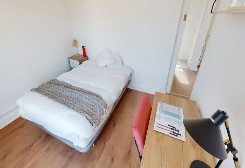 Camera da letto luminosa e ordinata con letto ben rifatto, comodino e scrivania con lampada — stile moderno, minimal e accogliente.