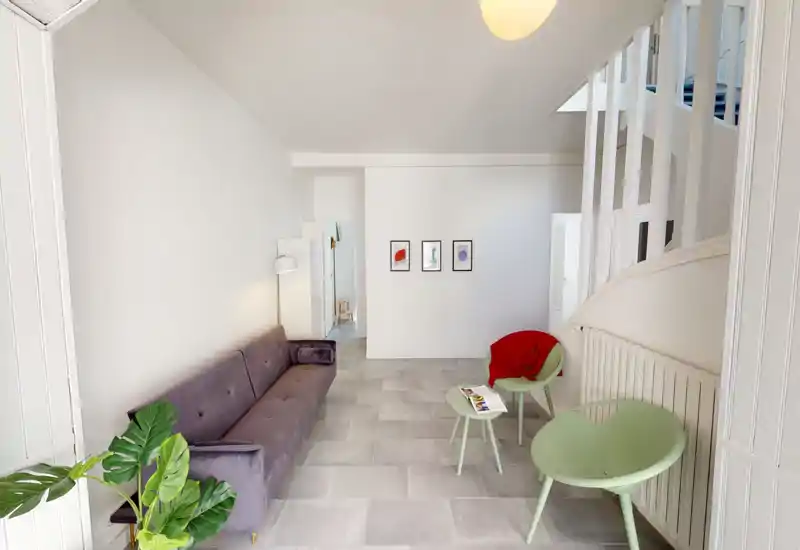 Soggiorno moderno e luminoso con un divano lungo imbottito, due poltroncine verde menta e tavolini; pareti bianche minimal e dettagli morbidi che rendono l'ambiente arioso e accogliente.