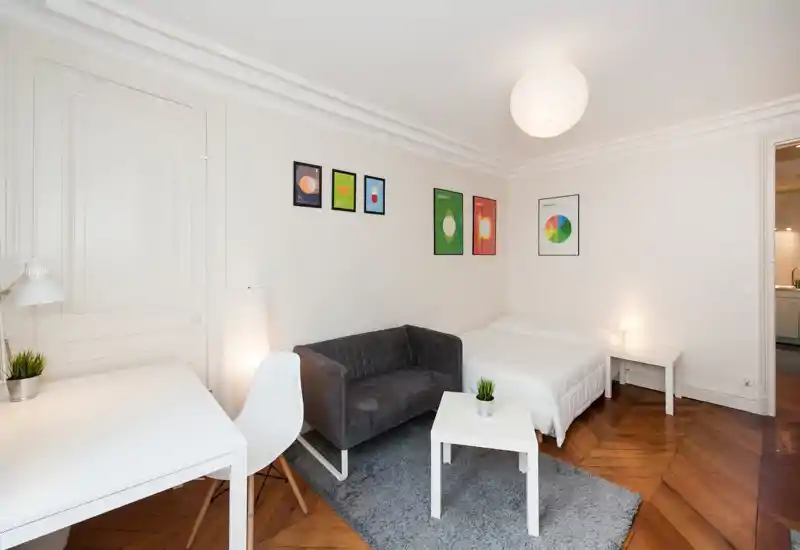 Bright and tidy studio bedroom with a double bed, small sofa, desk and tasteful wall art. Hardwood herringbone floors and soft rug add warmth to the minimal, modern decor.