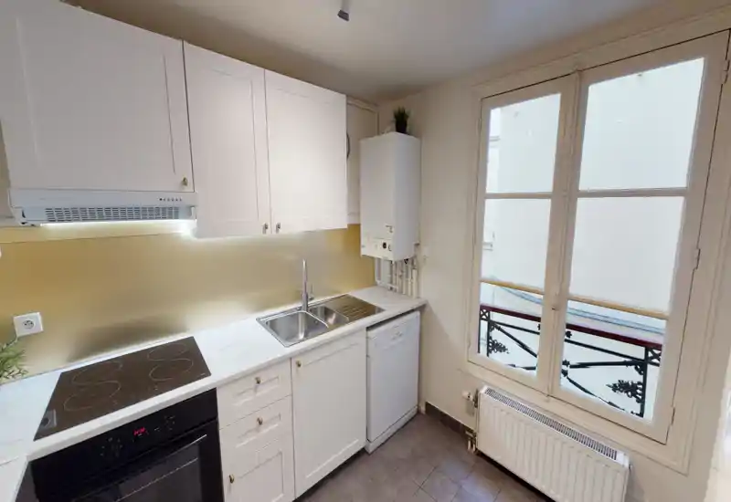 Bright, modern compact kitchen with white cabinetry, induction cooktop, double sink and dishwasher next to a large window that provides natural light.