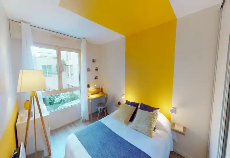 Camera da letto moderna e luminosa con letto matrimoniale, parete d'accento gialla e ampia finestra che porta luce naturale. La stanza dispone di mensole, una scrivania e tessili confortevoli.