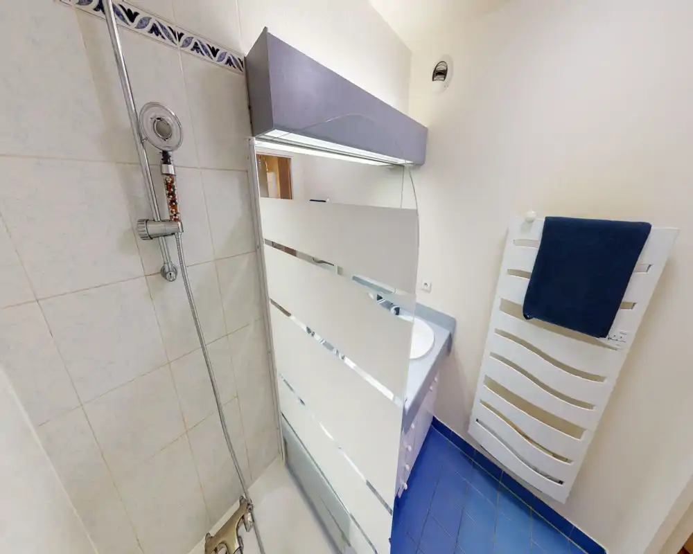 Bagno compatto e pulito con doccia, pannello in vetro parziale, lavabo con mobile e termoarredo per gli asciugamani. Ambiente luminoso e funzionale adatto a soggiorni brevi.
