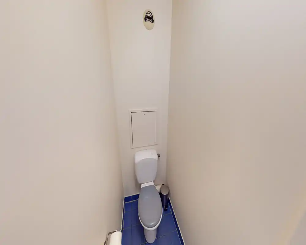 Toilet compatto con cassetta a muro, pavimento in piastrelle blu e pareti color crema neutro; semplice, pulito e ben illuminato.