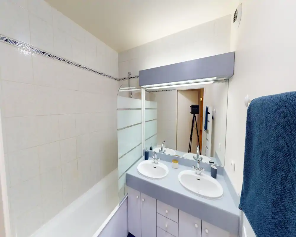 Bagno luminoso e pulito con vasca/doccia, doppio lavabo e specchio grande — ideale per soggiorni in famiglia.