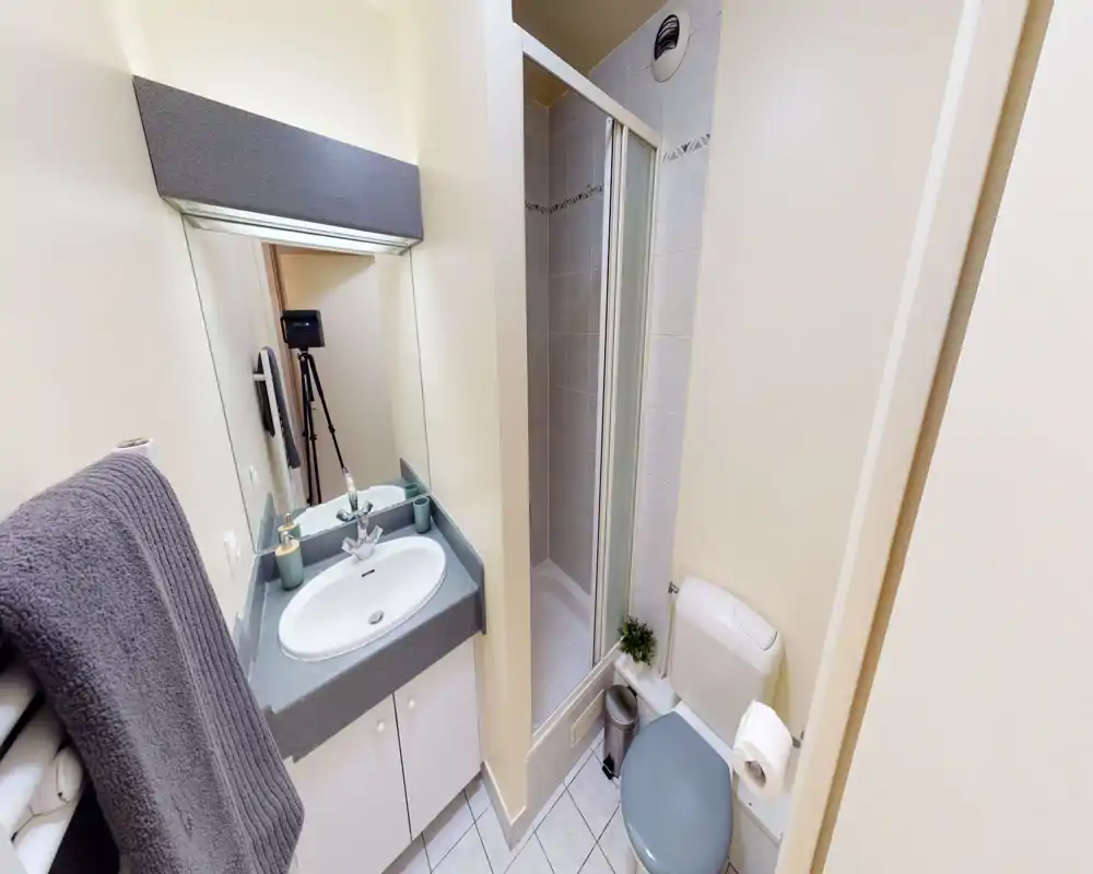 Bagno compatto e ben illuminato con lavabo, specchio, box doccia e WC; piastrelle neutre e accessori ordinati lo rendono pratico per gli ospiti.