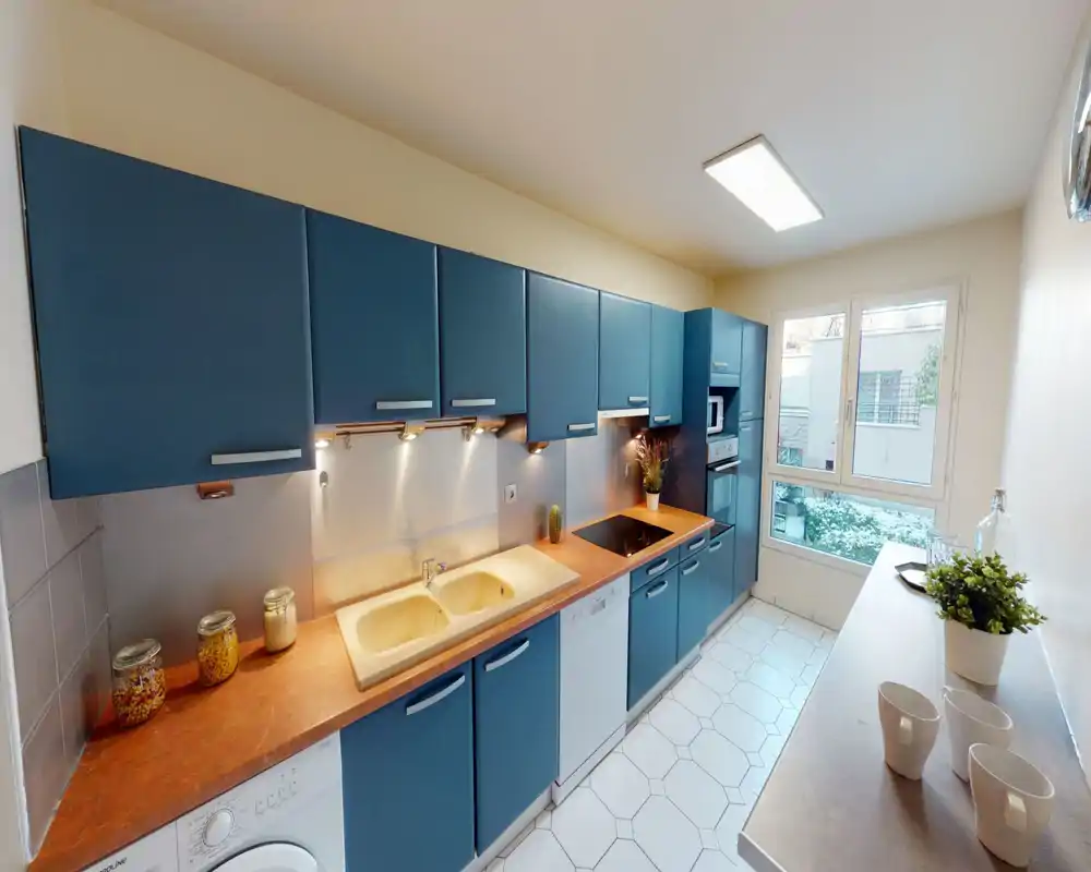 Cucina moderna a corridoio con pensili blu, elettrodomestici integrati, doppio lavello e finestra luminosa — ambiente elegante e ben illuminato perfetto per cucinare.