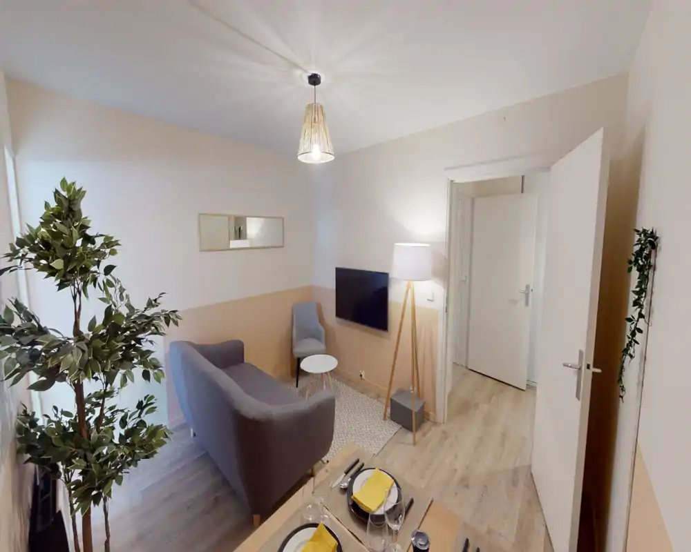 Soggiorno ben arredato con divano compatto, poltrona, TV a parete e illuminazione calda; tonalità neutre e piante creano un ambiente accogliente, perfetto per affitti brevi.