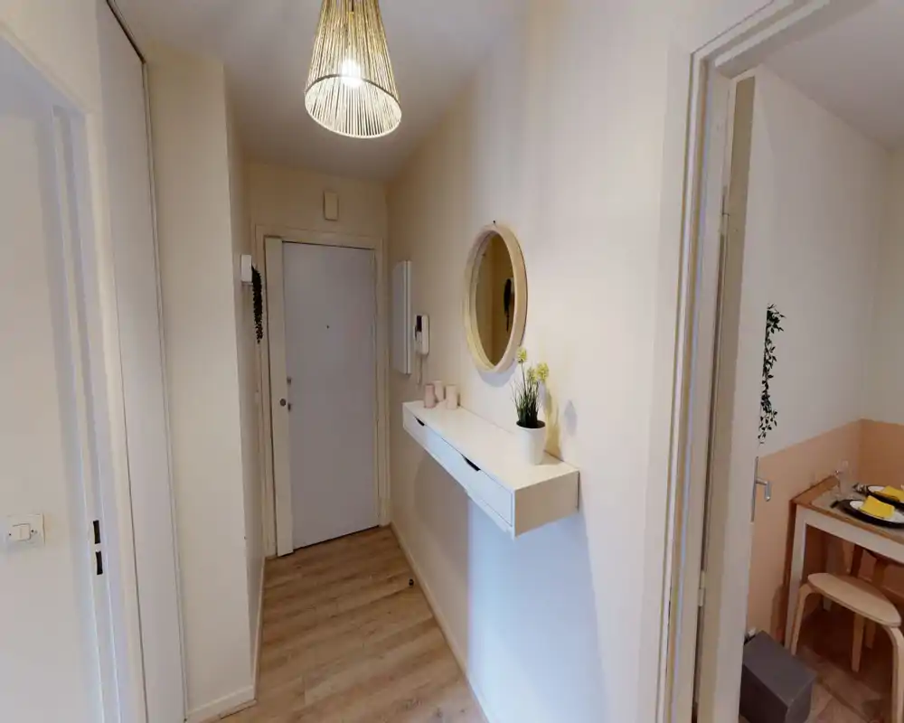 Ingresso luminoso e stretto con mensola a parete, specchio rotondo e lampada a sospensione; pavimento effetto legno e pareti chiare offrono una piacevole prima impressione.