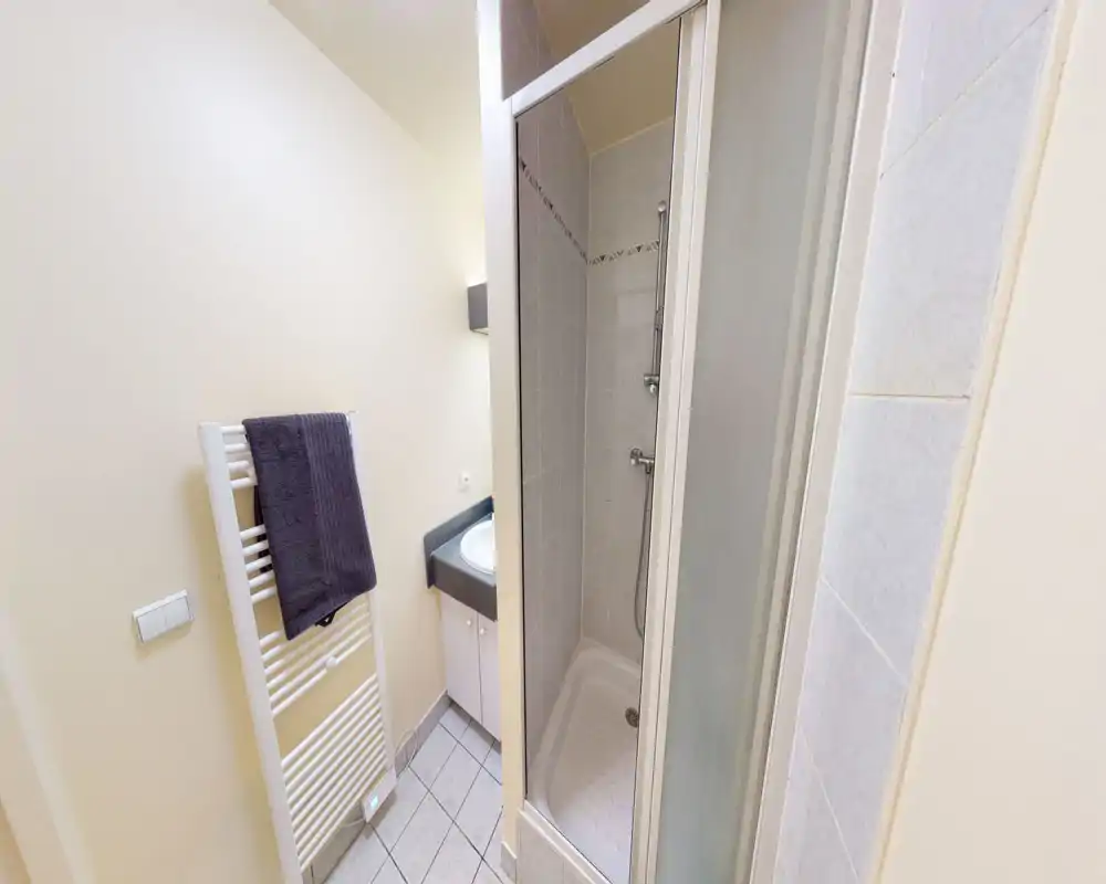 Bagno compatto con box doccia piastrellato, piccolo lavabo con piano e scalda-asciugamani. Spazio pulito e ben illuminato, ideale per soggiorni brevi.