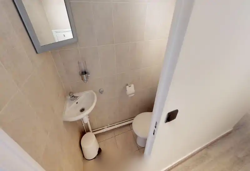 Compact, well-lit bathroom with a wall-mounted corner sink, toilet and tiled walls—neat and functional for a small guest WC.