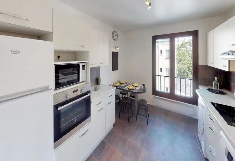 Bright, modern kitchen with integrated oven and microwave, a small dining nook by a large window, and white cabinetry creating a clean and airy look.