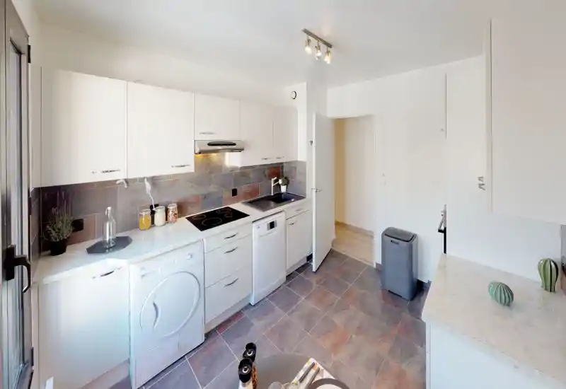 Modern, compact kitchen with white cabinetry, built-in cooktop and dishwasher, tiled backsplash and practical countertop space — bright and neatly styled for efficient cooking.
