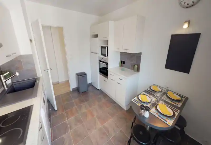 Compact modern kitchen with a tiled floor, integrated appliances and a small set dining table for two; bright, well-organized and ideal for short-stay rentals.
