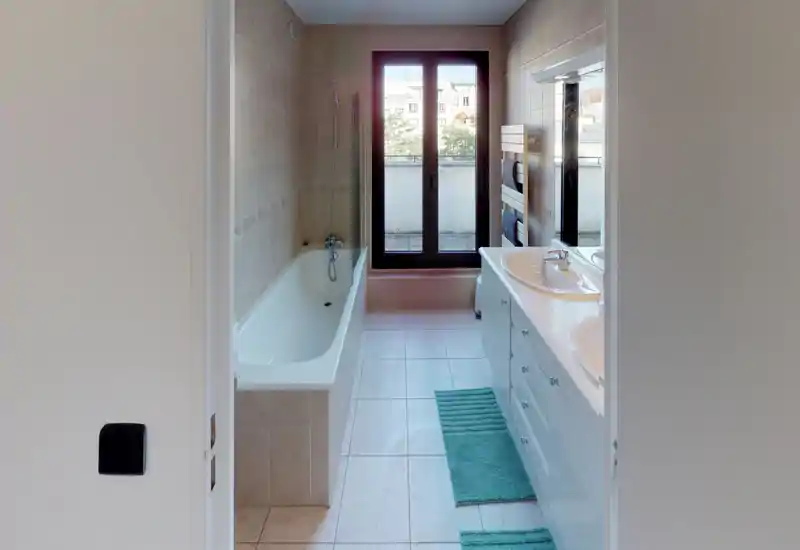 Bright, modern bathroom with a bathtub on the left, a double sink vanity on the right and a large window providing natural light.