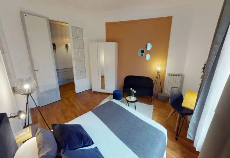 Bright, stylish bedroom with a large bed in the foreground, warm accent wall, seating corner and workspace by the window — ideal for rental listings highlighting comfort and design.